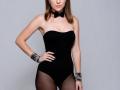 Jumiera in a black strapless bunny suit, black bowtie, and black sheer pantyhose, wearing silver wrist cuffs, with hands on hips, showing small tits and a slim ass.