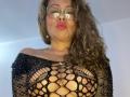 MiaAmoretti with curly brown hair, wearing glasses, and a black fishnet top that exposes her large tits and nipples, pouting her red lips.