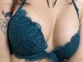 MoonLiza's tits in a teal lace bra, showing some cleavage and a tattoo of a woman's face on her right arm. Her skin is light, and she's wearing a black necklace.