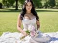 Hannu with big tits, wearing a white, strapless, corset-style wedding dress, sitting on a blanket, holding a bouquet of pink and white flowers, in a sunny park.
