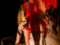 MiaMeowa with long blonde hair, naked, showing her ass, standing in red and black shadowed lighting, next to a white stone balcony. Red light casts a shadow on her.