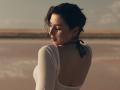 OliviaCluff has short, dark hair, a white long-sleeve top with a black halter, and a visible back with a slight tan, looking down with a soft expression.