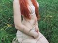SheritaChieng with red hair, white bra, and white panties, standing in green grass, holding her white panties down with her right hand, showing her pale, flat-stomach.