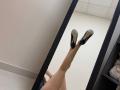MoonLiza's legs in black heels, reflection in a mirror, showing her ass and white soles, in a room with white walls and a black shelf on the right.