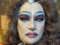 QueenOfPainSasha has red glitter eyeshadow, thick black eyebrows, curly brown hair, a nose ring, and pink lipstick. Her makeup is dramatic with bold eyeliner and shimmer.