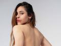 AntonellaReed's bare back, brown hair, nose ring, gold earrings, and slightly turned head showing her pouty pink lips, topless against a plain background.