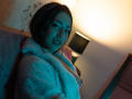 AnnFisher with blue-tinted skin, medium tits, and a fluffy white coat, sitting on a couch, looking at the camera with a slight smile, in a dimly lit room.