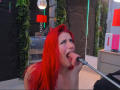 AlissaBrown with red hair is on her knees, sucking a cock with her eyes half-closed, looking up. She's nude, her tongue out, holding the cock with her hand.
