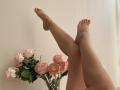MysteryLaddy's legs are crossed with pink-painted toenails, and a vase of pink peonies is below. Her bare ass is partially visible.