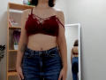 Steisii with small tits, wearing a red lace bra and high-waisted blue jeans, standing in front of a mirror, showing a tattoo on her right arm.