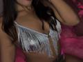 LexieBloom has small, shiny silver fringed bikini top covering her tits, with long brown hair and a subtle necklace, dark skin, and pink plush in the background.