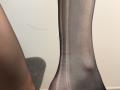 Tattiya's leg in sheer black pantyhose with a visible seam running down the side. The leg is slightly bent and the pantyhose are tight against her skin.