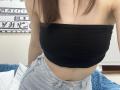 Ramilla has small tits, wearing a black tube top and light blue jeans, her brown hair falling forward. Her midriff is visible, and she's leaning slightly forward.