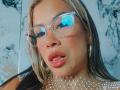AlixLow with reflective glasses, pouty pink lips, tongue slightly out, wearing a fishnet top and hoop earrings, blonde hair, light brown skin, and a confident, sexy expression.