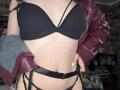 ClaireSpisak's tits in a black bra, wearing a red leather jacket, black strappy panties, with yellow nails, standing in a dimly lit room.
