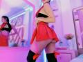 MelisaDaltonn in a red skirt, black top, and thigh-high socks with red bows, showing her ass in a mirror reflection. Her tits are small, her pussy is not visible.