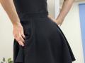 Rorria's black skirt, hands in pockets, shows a flared, textured, A-line design. Rorria's fingers slightly grip the skirt's fabric, with visible skin and nails.