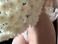 DominicaChambley's ass in pink lace panties, with a large bouquet of white chrysanthemums covering her upper body. Glass on a table in the blurry background.