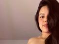 ViolettaRouse has long, dark hair covering one eye, smiling with pink lipstick, and a necklace, showing bare shoulders and a cute, slightly flushed face.