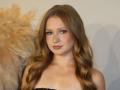 AkilahGhil has long, wavy blonde hair, blue eyes, and is wearing a black strapless top, showing her boobs. She's looking at the camera with a slight smile.