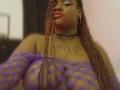 RoseBeckers with long braided hair, purple fishnet top revealing large tits, black choker with heart, and tattoo on chest, wearing gold hoop earrings, pouting slightly.