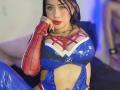 Kkole in a Spider-Man arm glove and blue latex superhero outfit with red webbing, showing big tits, red lips, and black hair, resting her chin on her hand.