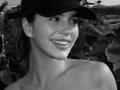PeacHub69 has a cute smile with white teeth, wearing a dark cap, and is topless with smooth shoulders. Black-and-white photo. PeacHub69's skin is slightly shiny.