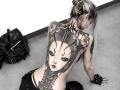 ErgoProxy's back is a massive black-and-white tattoo of a masked woman with floral and chain details. She's topless, wearing black leather gloves and pants, with a leather bag.