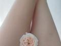 Les cuisses pâles de GladisBelle, les jambes croisées, avec une rose rose pâle entre ses jambes, révélant une peau lisse et une fleur délicate..