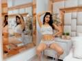 MelisaDaltonn, sitting on a chair, wearing white lace lingerie, her hands in her dark hair, her legs spread, revealing her pink pussy, in a mirror's reflection.
