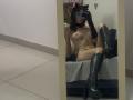 Valnes, nude, with cat ears, black gloves, and knee-high boots, sitting on a bed, taking a mirror selfie, showing small tits and a slim, sexy body.