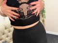 Stefanni's hands with red nails touch her black fishnet top, exposing her boobs through the lace pattern. She's wearing a black skirt, showing her bare midriff.