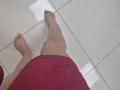 JoannaSia's bare legs and feet are on a white tiled floor, wearing a red skirt, with slightly dirty toes and a small black mark on her right ankle.