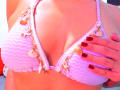 NalaLeroy's pink zigzag bikini with shell decorations, showcasing her tits, has red painted nails and a hand on her chest. Her skin is light.