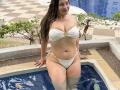 LorensDouce with wet brown hair, white bikini, showing her tits and pussy, sitting in a blue-tiled pool, smiling, hands on edge, checkered floor in background.