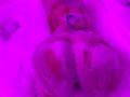 JuliaGarciax's butt is covered in pinkish soap suds, with a small tattoo visible on her lower back, lying on a white surface. Pink lighting fills the image.