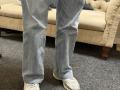 Dalaila's legs in blue denim jeans with white sneakers standing on grey carpet. Cream-colored tufted sofa in background.