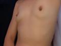 MilaHans' bare chest with small, perky tits and light skin, showing a single, dark brown nipple on the right side. Her arm is slightly visible on the left.