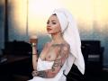 KayaBelle with a white towel on her head, holding a cup, showing off her tits and tattooed arm, looking confident. Her boobs are small, and she has a sexy look.