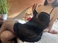Tisia with long brown hair, black lace lingerie, and fishnet stockings, holding a feather, sitting on a bed, showing her tits and ass. Stuffy toy in background.