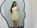 TrishMuhlbauer stands in a mirror wearing a yellow, floral, sleeveless dress that flares out, holding a phone with one hand, showing her ass and tits.