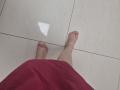 JoannaSia's bare feet with pink toenail polish on white tiled floor, wearing a red skirt, from a slightly lower angle.