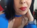 LauraSin with red lipstick, blue choker, and blue top, showing her tits, black hair, and silver wristwatch, in a selfie. Her face is slightly tilted to the right.