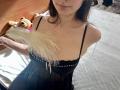 Tisia with a black sheer dress, holding a feather, showing her small tits and fair skin, brown hair, and a slight smile. Her ass is not visible.