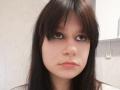 AlicaMihal has straight, dark brown hair, pale skin, and a serious expression with small, pinkish lips. Her brown eyes are slightly upturned. She's wearing a white shirt.