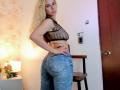 SophieTeller with blonde hair, wearing a sheer black polka dot top and tight blue jeans, showing her big ass and small tits, standing in a room.