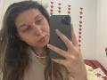 Sanella's selfie shows her with wavy brown hair, light skin, and a pearl necklace, holding a green phone, wearing a white shirt, with a subtle smile.