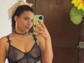 LucieMilner with tan skin, dark hair in a bow, wearing sheer navy bra, exposing small tits, choker, red nails, holding phone, mirror selfie, brown door in background.