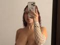ValeryScot with curly red hair, pouty lips, holding phone, wearing white fishnet arm, showing large tits, no clothes, gold necklace, in mirror selfie.
