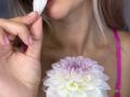 MikyWayxy's hand holds a white dahlia, touching her pink-lipped mouth with the flower. She's got blonde hair, pink bra straps, and pale skin, with her tits visible.